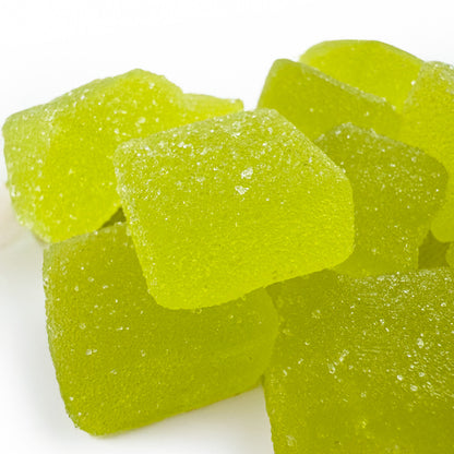 Zoom d'un tas de gummies au THC verts goûts pomme sur fond blanc